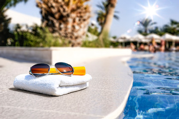 Summer sunglasses and white towel with swimming pool space 