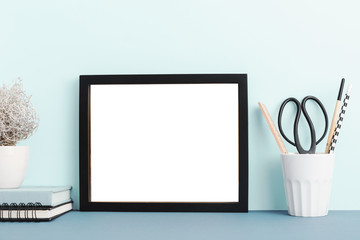 Empty frame on  a desk with blue wall. Mockup.