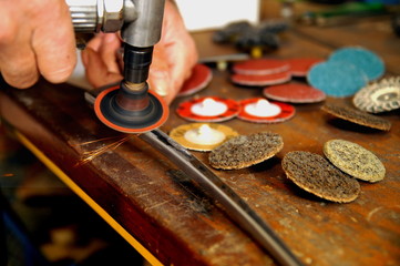 Obraz premium A man working with air pump grinder cleans metal parts blanks. close up on tool, hands, Grinding and polishing wheels and sparks. real situation picture