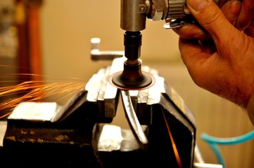 A man working with air pump grinder cleans metal parts blanks.  close up on tool, hands and sparks....