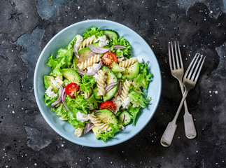 Mediterranean pasta avocado salad on a dark background, top view. Vegetarian diet food concept