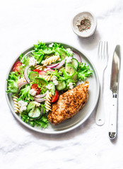 Mediterranean avocado pasta salad and baked chicken breast - healthy balanced lunch on a light background, top view
