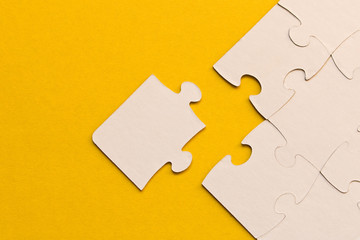 White jigsaw puzzles on yellow background. The concept of development of thinking. The concept of teamwork.