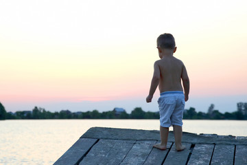 small child stands on the pier near the water