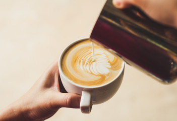 Closeup image of female barista holding and pouring milk for prepare cup of coffee, latte art,...