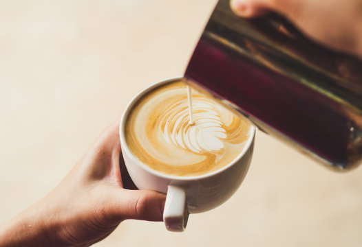 Closeup image of female barista holding and pouring milk for prepare cup of coffee, latte art, vintage color tone, coffee preparation and service concept, lifestyle