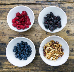 round white ceramic bowls with berries and nuts on a rustic wooden table
