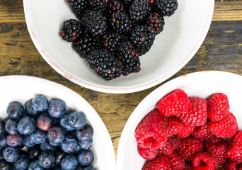 fresh organic raspberries and blueberriesand blackberries in white bowls on a brown wooden table