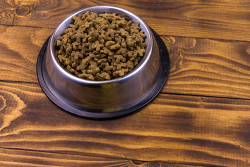 Dry cat food in bowl on wooden background. Pet food on wood surface
