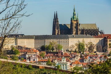 Prague, Czech Republic / Europe - April 22 2019: View of Hradcany and St Vitus cathedral from Petrin hill overlooking historical buildings with red roofs. Spring sunny day, blue sky, green trees.