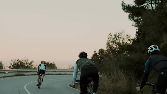 Group of road cyclists or three teammates cruise down empty sunset road during training or weekend ride. Slow motion epic and cinematic shot of athletic young people excercising in free time