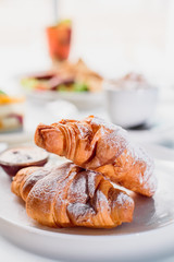 Beautiful fresh French croissants with jam on a white plate on a light background in the restaurant. Close-up. Space