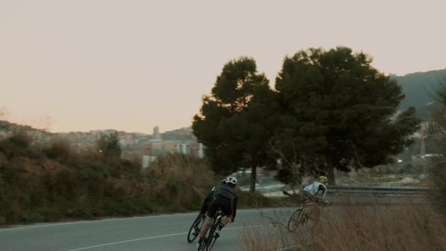 Slow motion of three cyclists descend down mountain road during golden hour, beautiful warm summer sunset. Group training and team work. Cinematic professional shot of healthy sport lifestyle