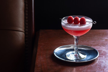 Clover Club Cocktail, a Sour Drink with Gin, Raspberries, and Egg White Foam in a Dark Luxurious Bar with Copy Space
