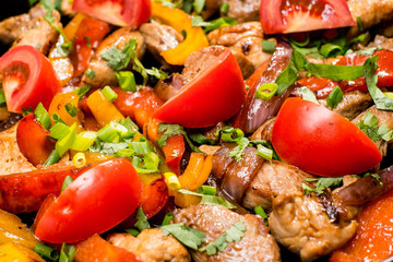 roast meat with potatoes decorated with fresh vegetables in a cast iron pan