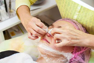 A young girl is lying on a couch during cosmetic procedures with a mask on the face above which...