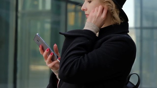 nice girl in black hat listens to music on phone in street