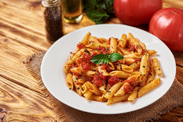 Penne pasta in tomato sauce with basil on a wooden table. The concept of Italian cuisine.