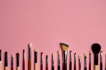 Different professonal makeup brushes lying below on a pink background. Copy space above. Top view. Close up. 