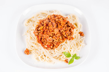 Spaghetti bolognese on a plate decorated with fresh basil in a white background