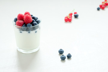 Joghurt im Glas mit gemischten Beeren auf weißem, strukturiertem Holztisch im Gegenlicht