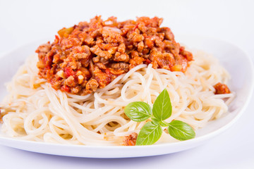 Spaghetti bolognese on a plate decorated with fresh basil in a white background