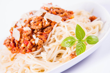 Spaghetti bolognese on a plate decorated with parmesan  cheese and fresh basil in a white background