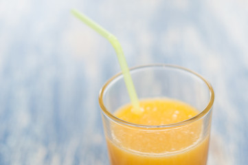 Orange juice in a glass with a straw on a blue wooden background of aqua color, top view and side view close-up