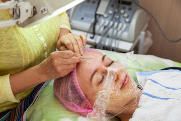 A young girl is lying on a couch during cosmetic procedures with a mask on the face above which...