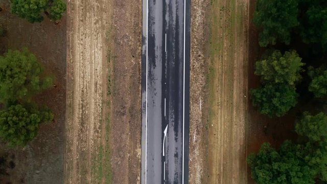 Aerial top view from drone on textured old asphalt paved tarmac road stretching in middle of forest, small hybrid or electric car drives to travel destination. Concept logistics