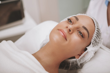 Obraz na płótnie Canvas Young beautiful woman with flawless skin receiving facial treatment at beauty clinic. Cheerful female client visiting cosmetologist. Attractive woman getting skincare therapy at cosmetology salon
