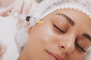 Cropped shot of a beautiful woman getting rejuvenating facial injections at cosmetology clinic. Professional beautician doing hyaluronic acid injections into female patient face. Youth, skincare conce