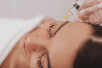 Top view shot of a beautiful woman smiling, receiving rejuvenating face injections at cosmetology...