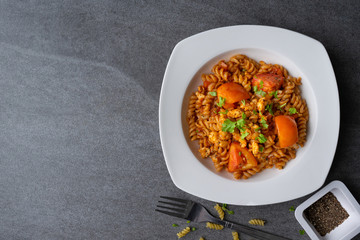 Spiral pasta in sauce tomato with chicken in white dish on concrete table.