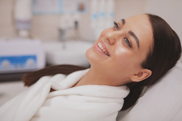 Beautiful happy woman with glowing healthy skin relaxing at cosmetology clinic, copy space. Attractive cheerful female enjoying pampering day at spa beauty center. Wellness concept