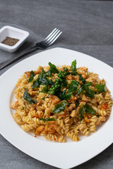 Spiral pasta in fried basil with chicken in white dish on concrete table.