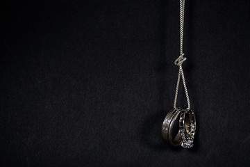 pair of wedding rings hanging from a silver chain with knot isolated on black background