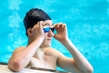 A teenage athlete improves swimming goggles in an indoor pool. Close up, selective focus.