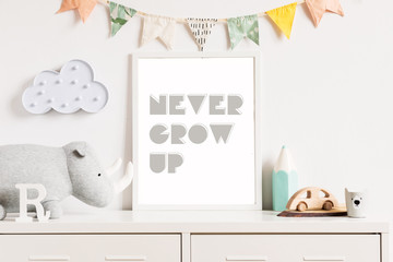 The modern scandinavian newborn baby room with mock up poster frame, wooden toy, plush rhino, accessoreis and clouds. Hanging cotton flags. Minimalistic and cozy decor of childroom. Mock up concept.