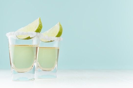 Tequila Shot Drinks With Green Lime, Salty Edge In Modern Pastel Green Interior On White Wooden Table.