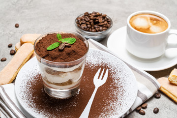 Classic tiramisu dessert in a glass and cup of coffee on concrete background