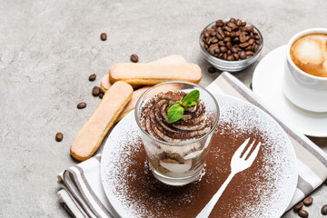 Classic tiramisu dessert in a glass and cup of coffee on concrete background