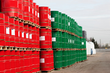 Barrels of 200 liters of metal are in the pallet on the street under the open sky. Red and green barrels for petroleum, chemicals, gasoline.