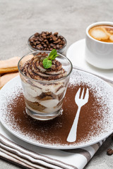 Classic tiramisu dessert in a glass and cup of coffee on concrete background