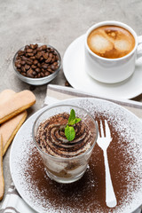 Classic tiramisu dessert in a glass and cup of coffee on concrete background