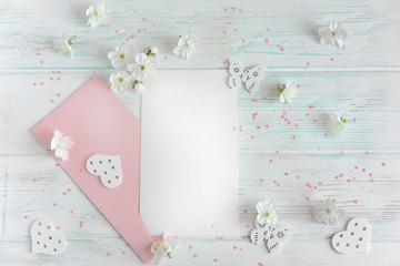 Mock up letter for greeting inscription. A letter on a light wooden background with a pink envelope and spring flowers of the cherry tree.