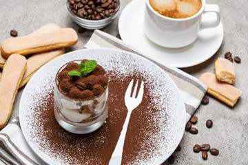Classic tiramisu dessert in a glass and cup of coffee on concrete background