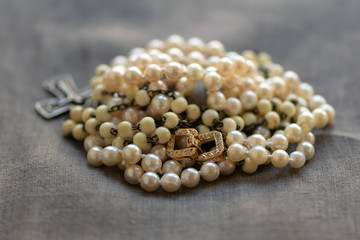 White rosary and pearl necklace on linen fabric. Luxury and modesty.