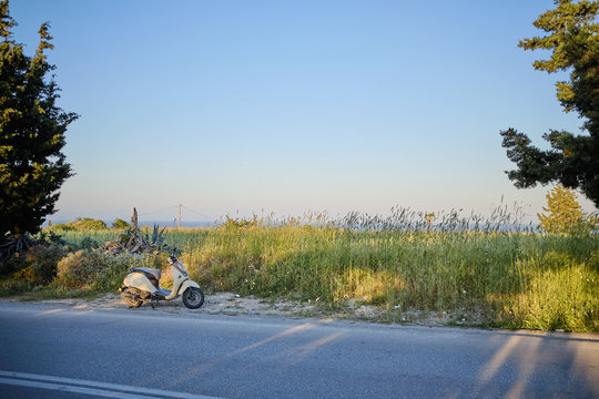 scooter parked along the road, green field in the background