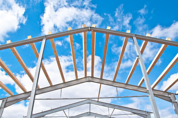 Metal frame of the new building against the blue sky with clouds. Metal frame of the building for further insulation. Wood beams and metal frame of the new building. 